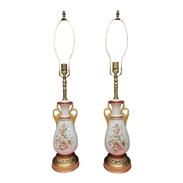 Mid-Century White Floral Porcelain Table Lamps - a Pair: This exquisite pair of mid-century lamps features a graceful white porcelain body, elegantly accented by ornate gilt scrolled handles. Hand-painted pink flowers blossom across the front, adding a touc