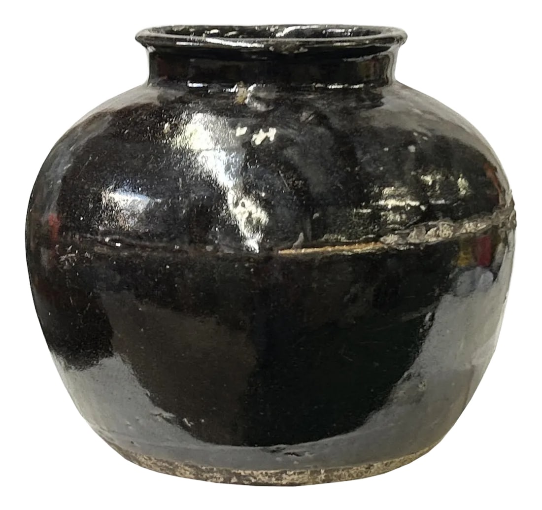 Vintage Earthy Rustic Black Village Rural Pottery Ceramic Pot Vase: The is a stout ceramic jar with a rounded body that tapers towards a narrow, slightly everted rim. The upper portion of the jar is covered in a glossy, dark rustic black glaze with subtle variations