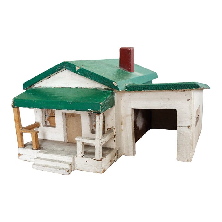 Vintage Handmade Folk Art House Model With Green Roof: A handmade folk art model of a small house with porch, chimney, and attached garage, painted in white with a green roof and red chimney. Its handmade construction and naïve proportions are