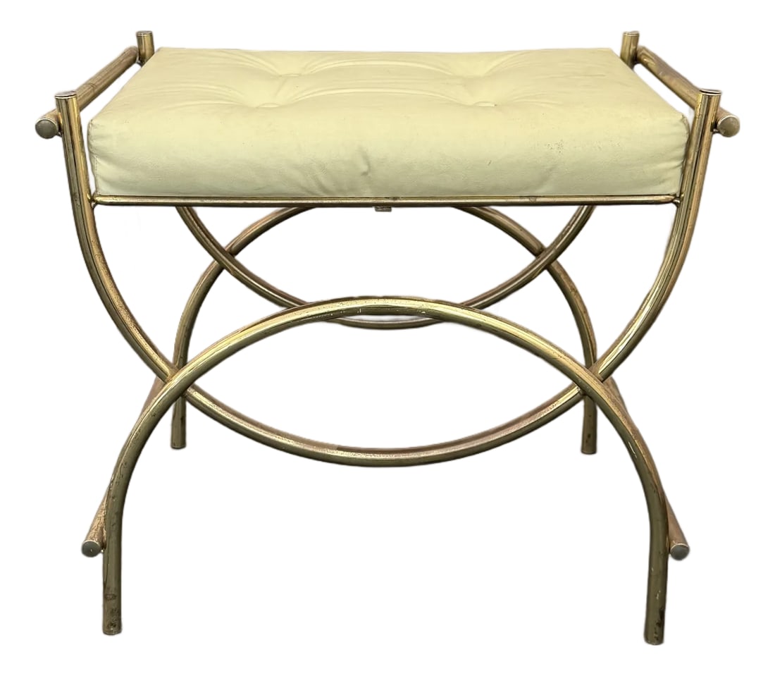 Hollywood Regency Brass Toned Tufted Vinly Curule Vanity Stool: This decorative Hollywood Regency vanity stool features a sweeping, brass toned frame that follows the format of an ancient Roman Curule stool with an x-base supported by crescent stretchers. The stoo