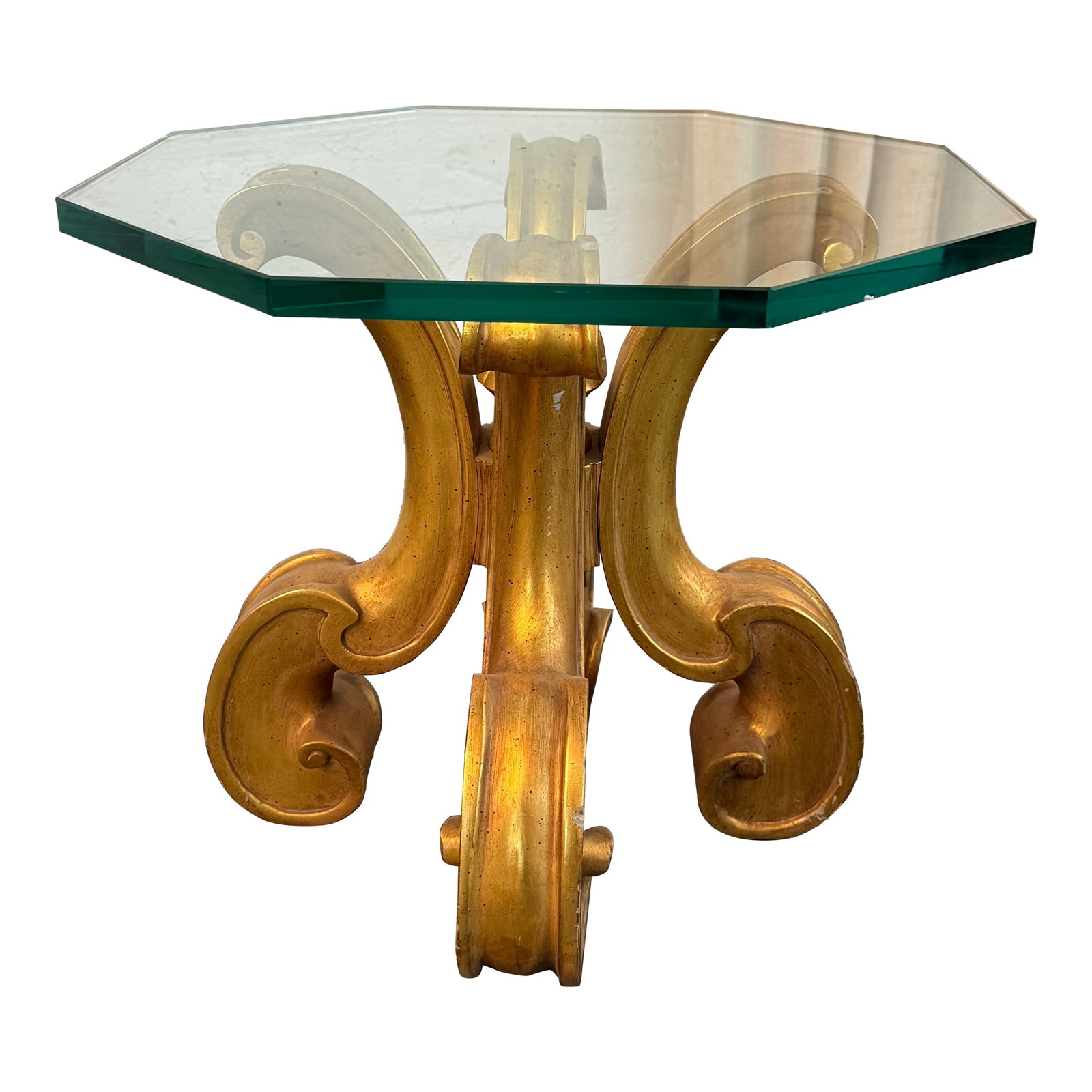 Late 20th Century Hollywood Regency Scrolled Gilt Octagonal Glass Side Table: This exquisite 1970s Hollywood Regency side table showcases an artisan, hand-carved wood pedestal base finished in a striking gold gilt. The architectural base features dramatic, interlocking