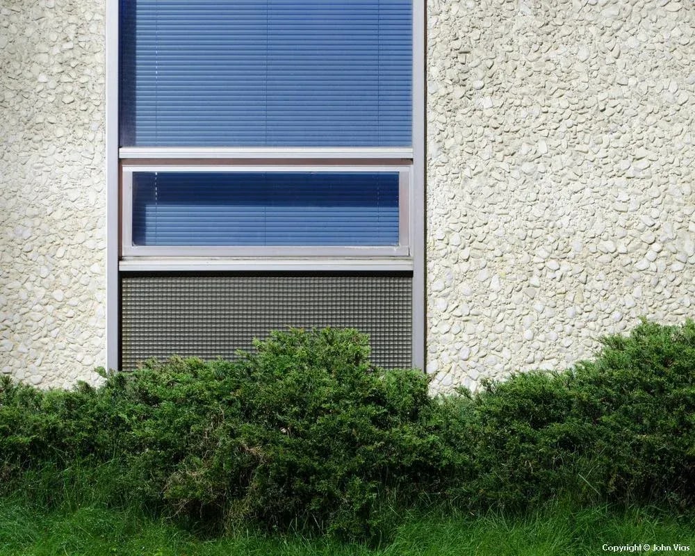 Contemporary Night Photograph "Blind" by John Vias: Note from the artist, John Vias: "As with certain other images, I like the rough, hard surfaces of the blind and wall contrasted with the softness of the grass and hedge." This 11" x 14" archival