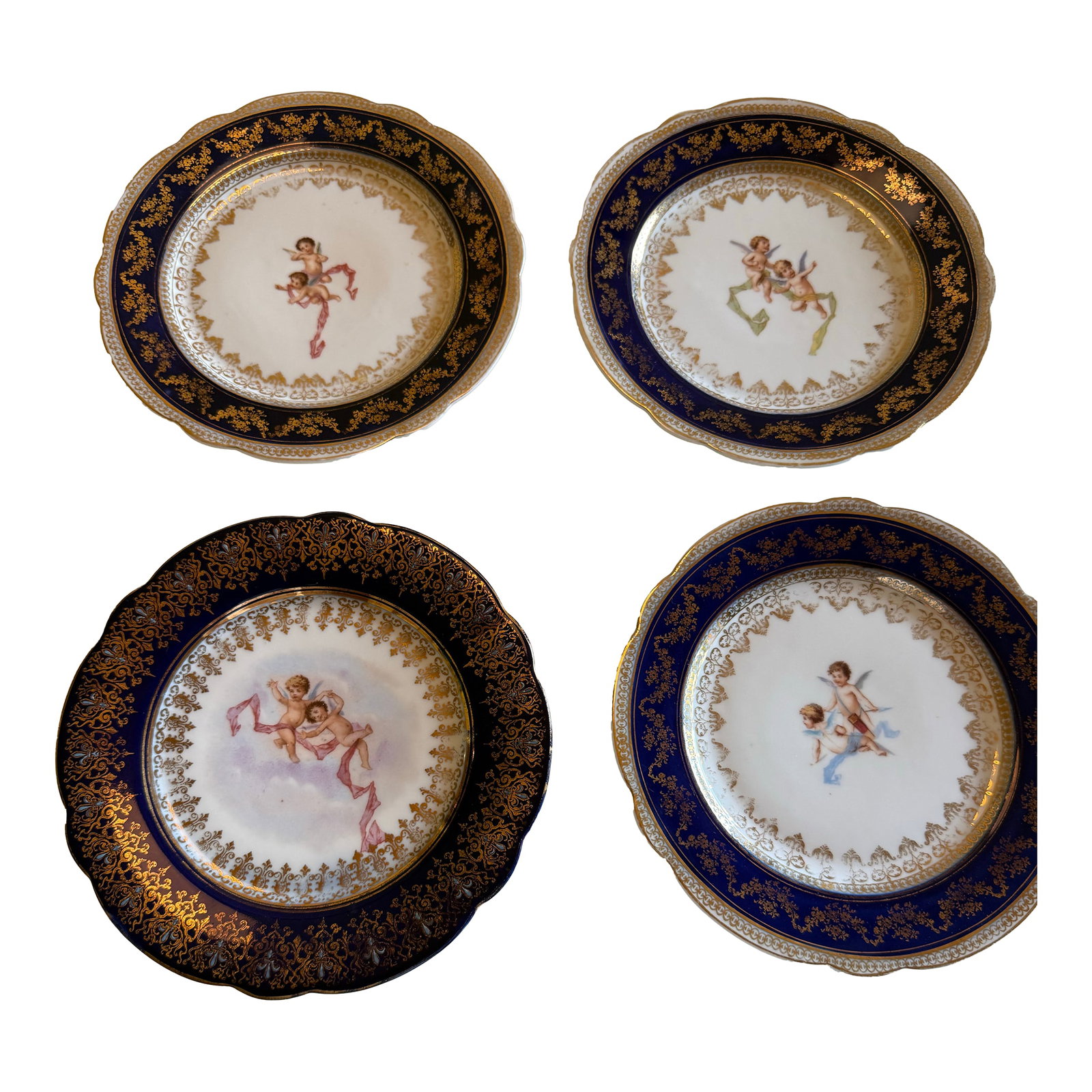 Antique Victoria Carlsbad Austria Cobalt & Gilt Cherub Cabinet Plates – Set of 4: A charming set of four antique porcelain cabinet plates by Victoria Carlsbad, Austria, dating to the late 19th/early 20th century. Each plate features a hand-painted central reserve depicting playful 