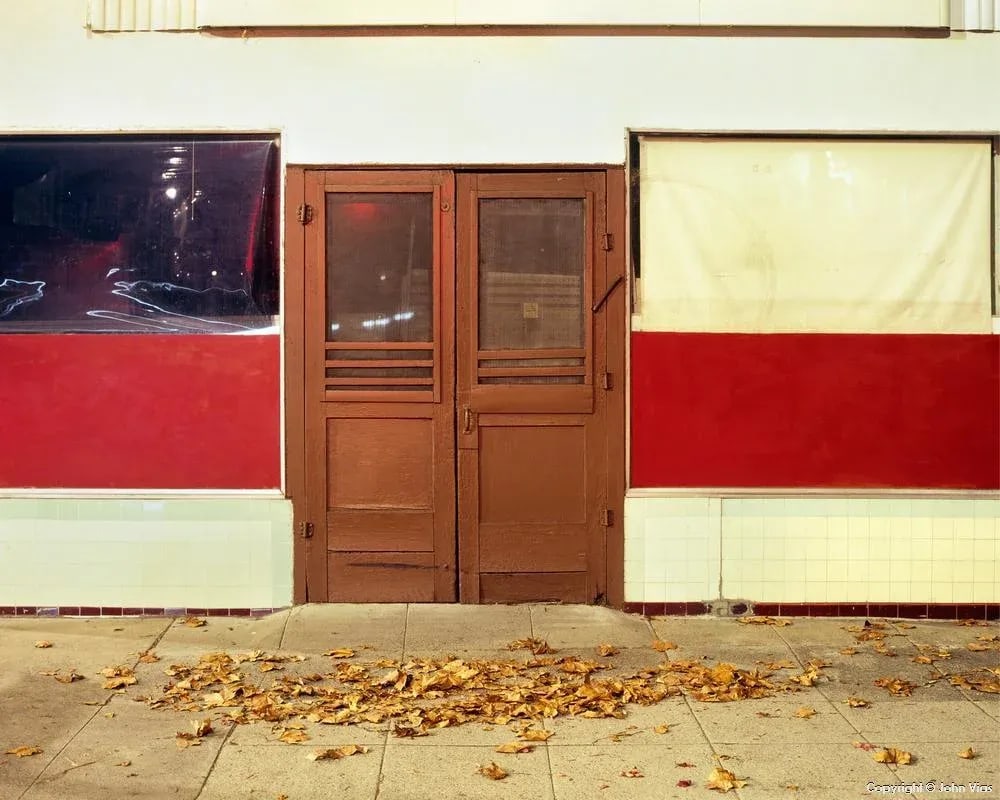 Contemporary Night Photograph "Flat-Front Building" by John Vias: Note from the artist, John Vias: "I have photographed this building at night many times, usually from farther away. The fallen leaves add interest and soften the straight lines and angles." This 8" x