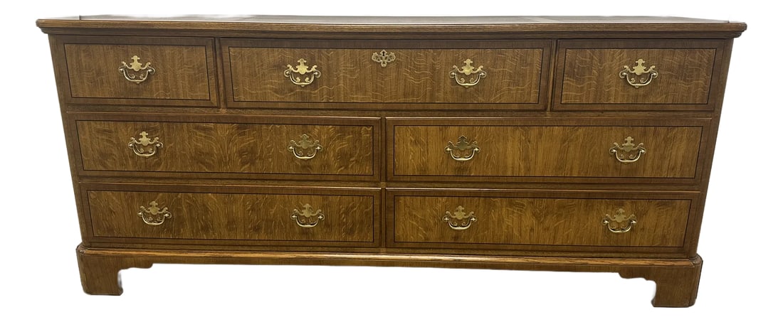 1980s Baker Furniture Georgian Oak Dresser: A stunning seven-drawer chest by Baker Furniture. Constructed of tiger oak with black lacquer inlay along the perimeter of each drawer and finished with beautiful brass hardware in the Georgian