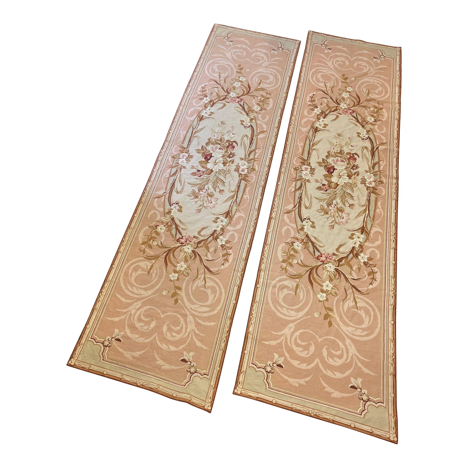 100% Wool Hand Knotted French Aubusson Pair of Runners in Muted Cream/Peach/Pink Floral Pattern: This elegant pair of hand-knotted 100% wool Aubusson runners is decorated in muted pastels with a central oblong medallion featuring depictions of flora and streamers, bordered with the same. The