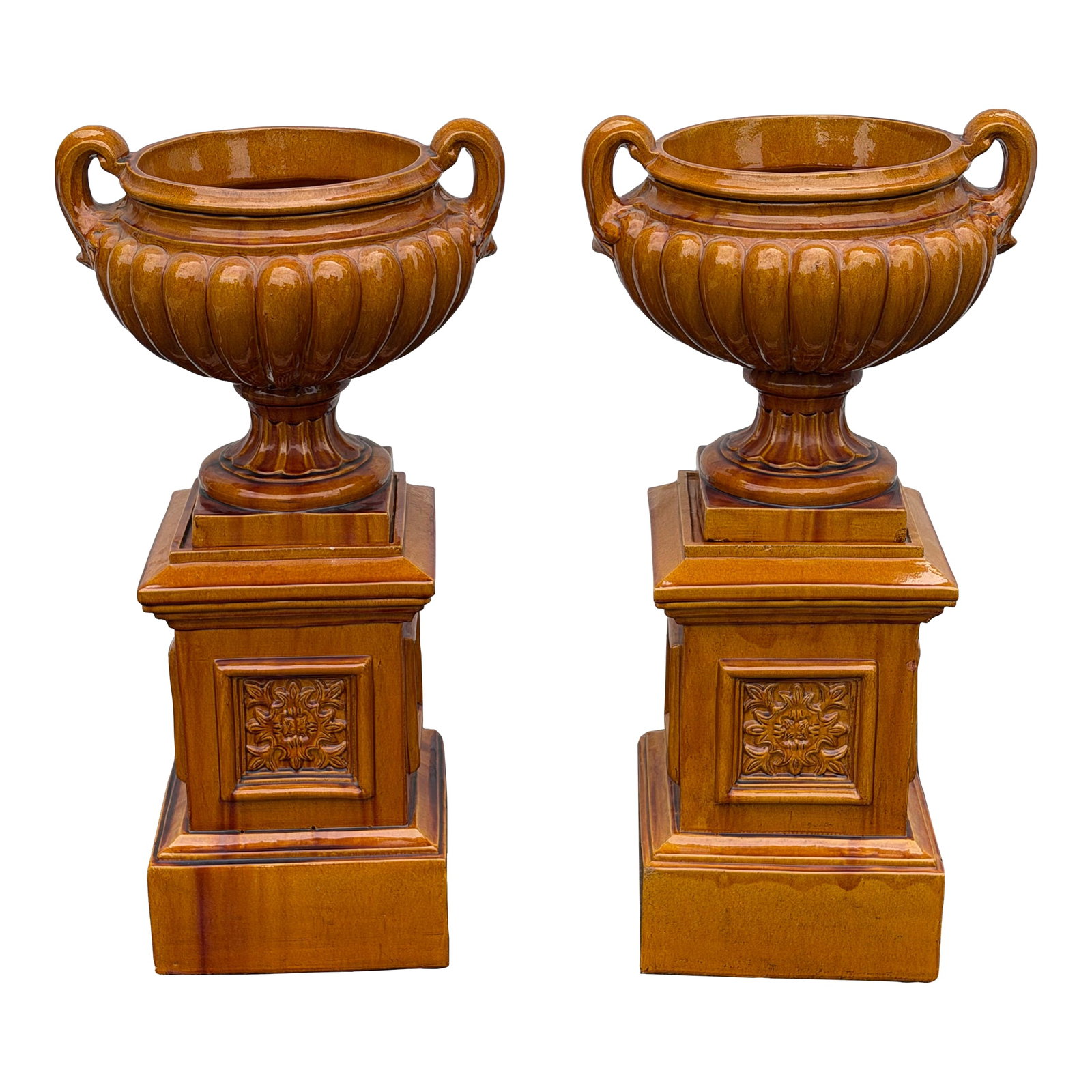 Monumental Glazed Ceramic Campana Urns on Pedestals 42" a Pair: A striking pair of large-scale campana-form garden urns, each set atop a matching square plinth pedestal, finished in a rich amber-ochre flambe glaze with warm caramel and burnt sienna tonal
