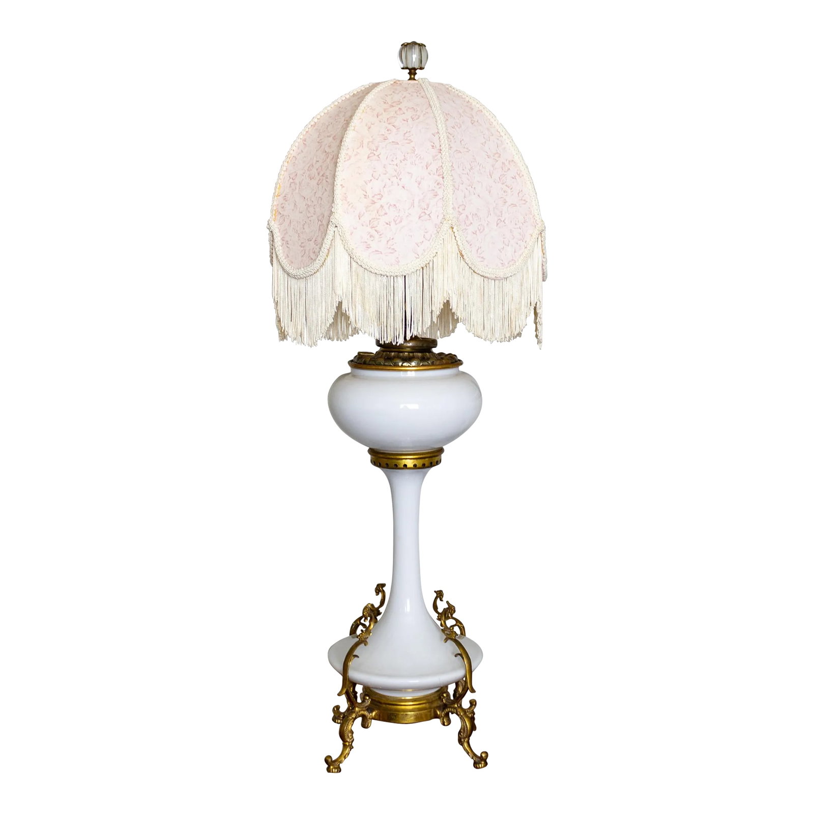 Electrified White Milk Glass Oil Lamp on Ormolu Feet | Fringed Lampshade: An French antique white milk glass lamp sits on an ornate brass ormolu-footed pedestal stand. It has two pull-chain sockets and a decorative round glass finial cupped by flower-shaped brass caps. We'v