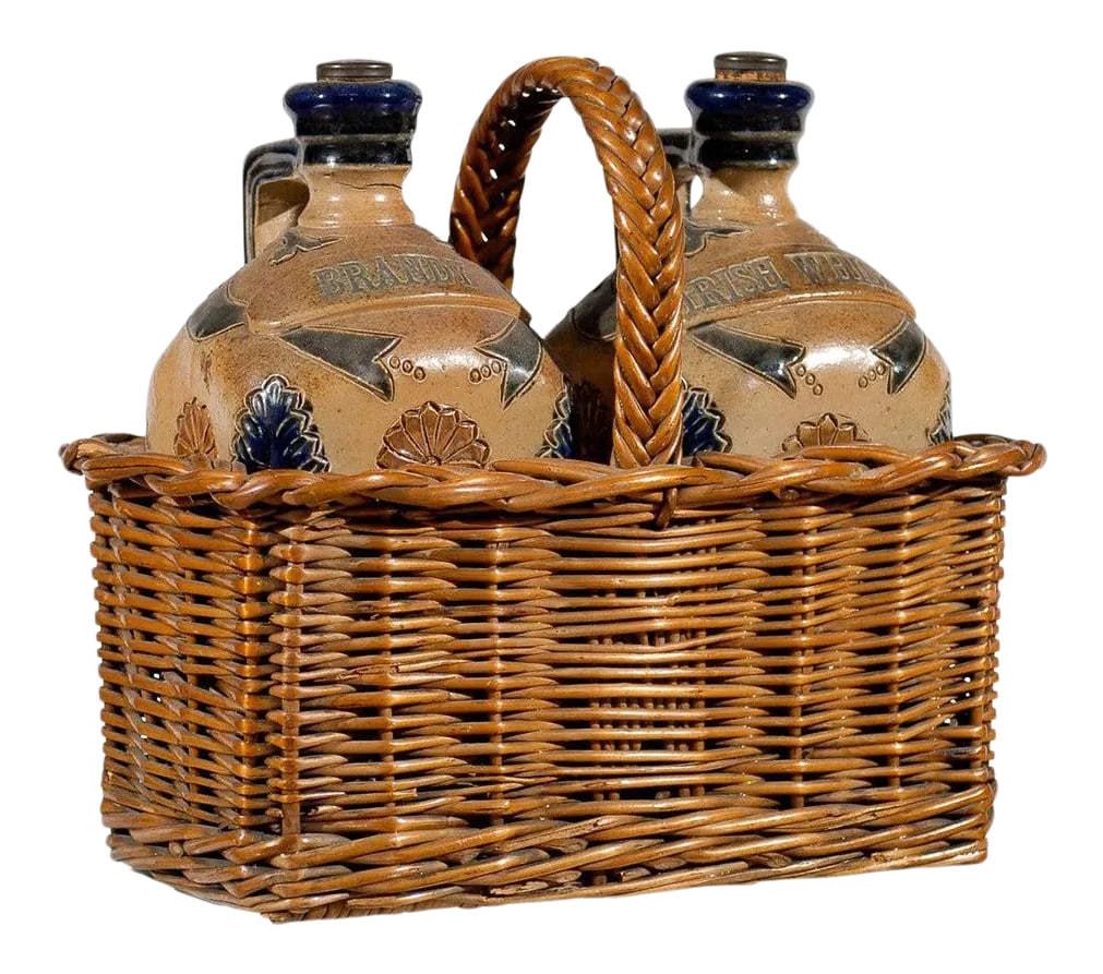 Antique Victorian English Pottery Decanters in Tantalus-Inspired Wicker Basket- 3 Pieces: Two English pottery decanters in a tantalus inspired wicker basket from the mid 19th century. Born in England during the Victorian period, this pair of decanters is set inside a tantalus-inspired