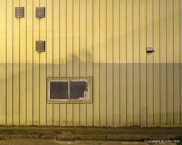Contemporary Night Photograph "Corrugated Wall" by John Vias: Note from the artist, John Vias: "I like the neat arrangement of windows, vents, and rivets juxtaposed with the imperfect paint job." This 8" x 10" archival color photograph is presented in a 20" x 16