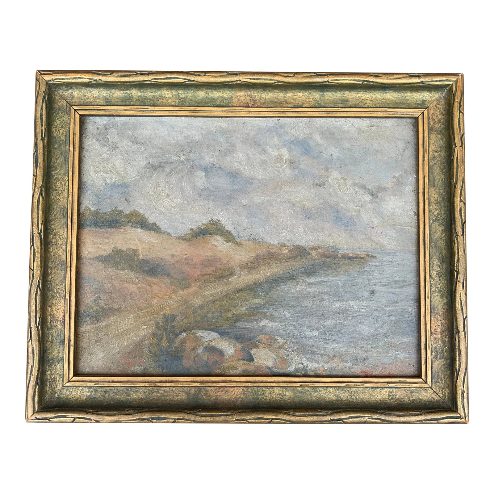 Early 20th Century Framed Coastal Landscape Oil Painting: An intimate early 20th-century coastal landscape painted in oil on board, depicting a gently curving shoreline beneath an expansive, cloud-filled sky. The subdued palette of misty blue, weathered gree