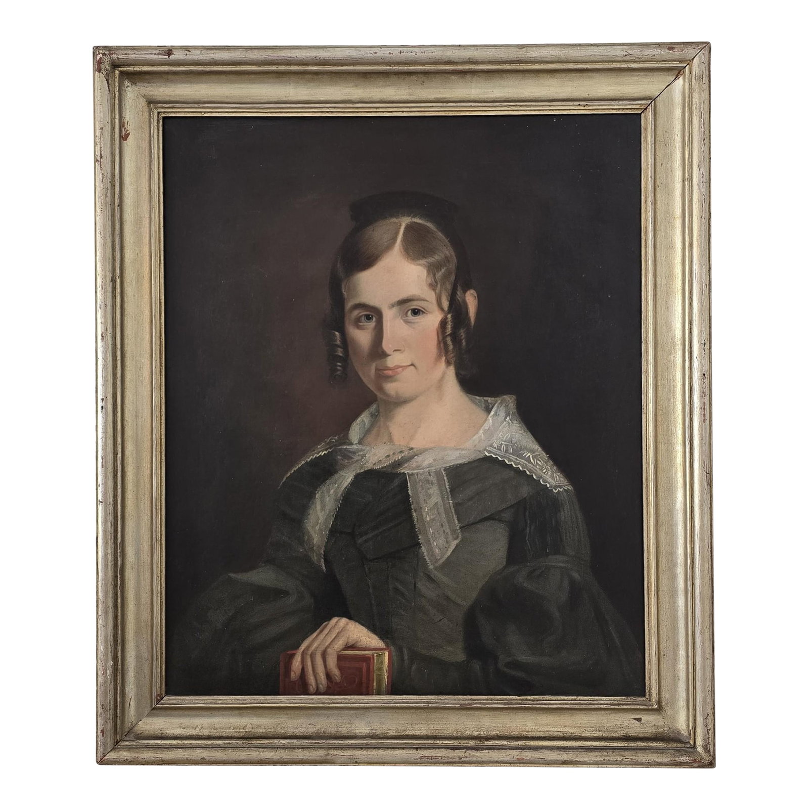 Antebellum American Oil Portrait on Canvas of a Young Woman, Circa 1835-1850: This antique American oil portrait on canvas dates to the early-mid 19th century (circa 1835-1850) and depicts a young woman posed against a dark ground, her hand resting on a book. The sitter's hairs