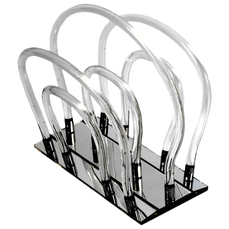 Lucite, Chrome & Mirror Magazine Stand After Dorothy Thorpe: In the manner of Dorothy Thorpe, this sculptural magazine rack has a mirrored base that holds twelve chrome sockets into which the Lucite uprights are secured. Condition: Alterations: Original
