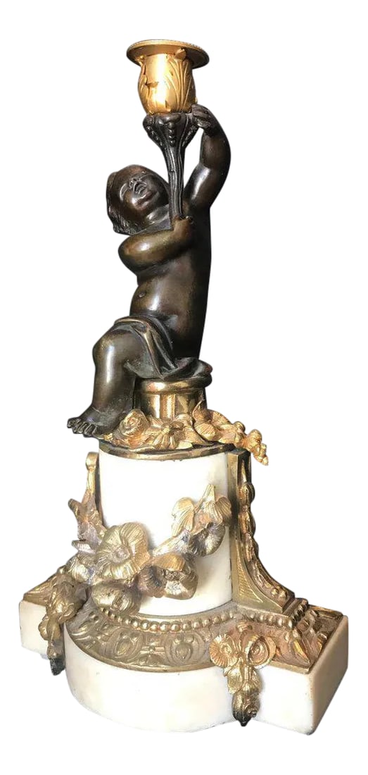 Louis XVI Style Putto Ormolu Patinated Bronze and Marble Candlestick: This French candleholder, in the style of Clodion, is mounted on white statuary Carrara marble. The patinated putto holds a candle support of flowering acanthus leaves. Circular and rectangular marble