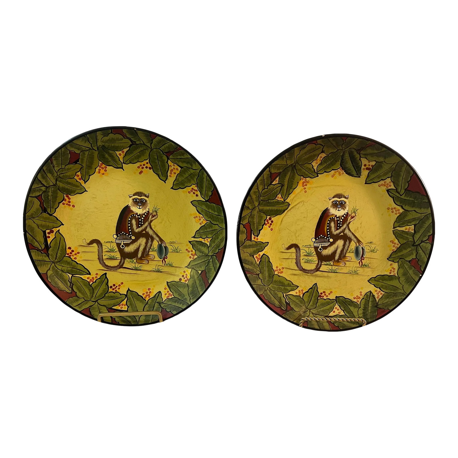 Vintage Palm Beach Regency Hand Painted Monkey Decorative Plates Decor - A Pair: . These plates feature a delightful scene of a whimsical monkey holding a blue hat, set against a backdrop of a golden yellow background. Surrounding this charming centerpiece is a border adorned