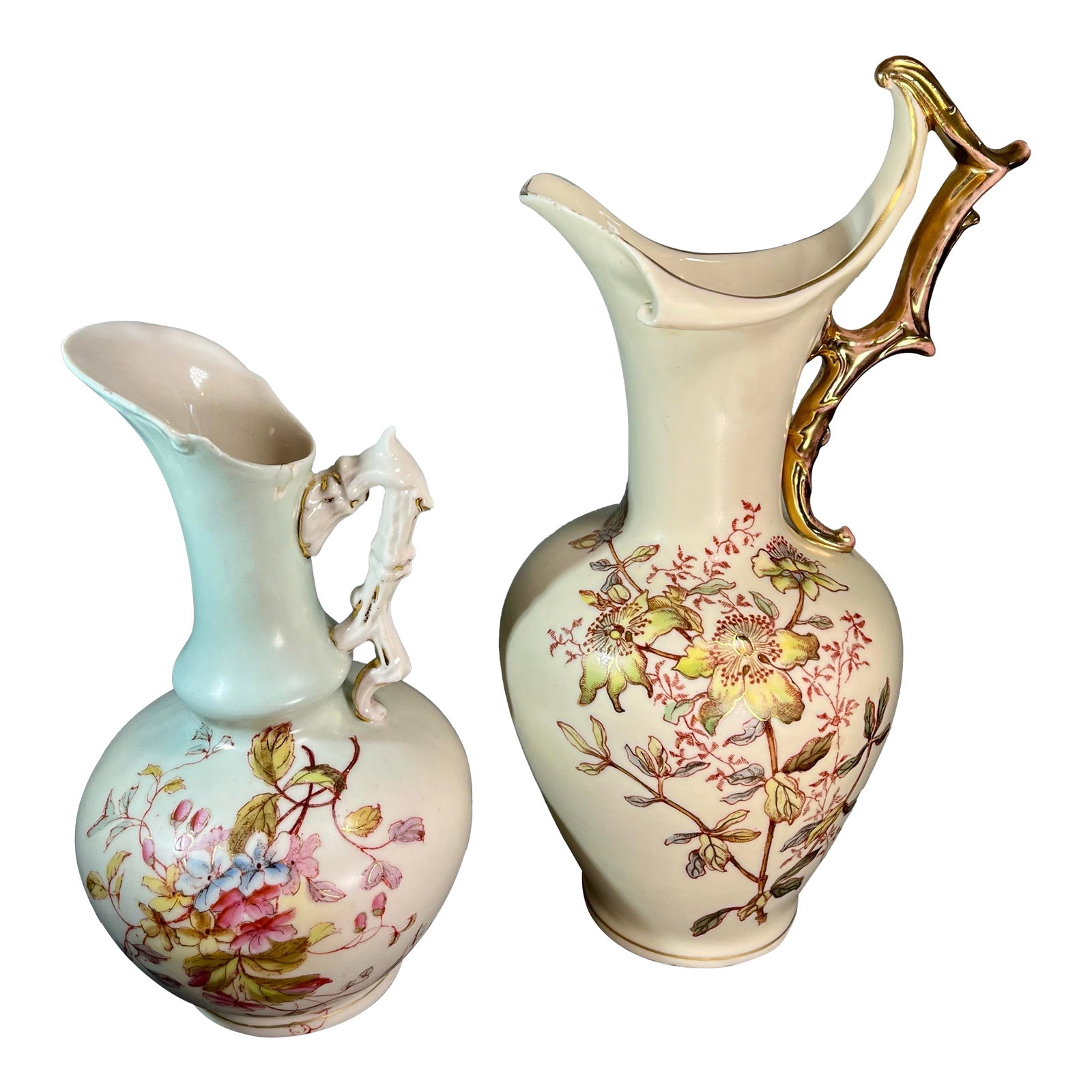 Late 19th Century Hand Painted Porcelain Ewers With Gilded Handles- 2 Pieces: A pair of porcelain ewers, possibly Royal Worcester, each exhibiting intricate floral decoration and elaborate gilt-accented branch-style handles. The larger ewer (10"H) features a cream-colored body 