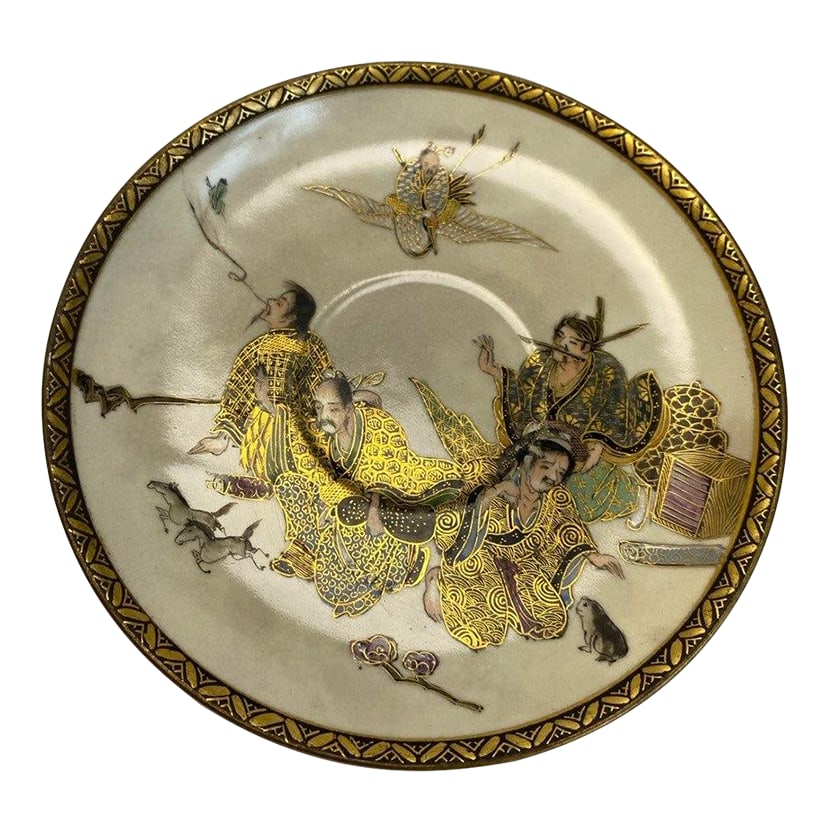 Japanese Satsuma-Style Plate With Four Figures & Gilt Decoration: This finely detailed Japanese plate features a narrative scene of four robed figures gathered beneath a flying immortal, rendered in soft enamels and delicate gilt. The figures are animated yet restra