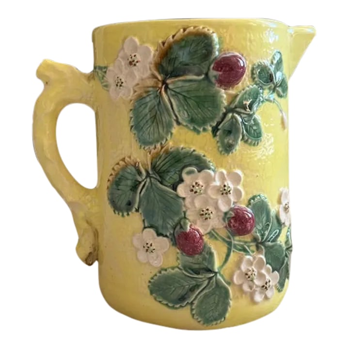 Antique Majolica Strawberry Pattern Water Pitcher: 7 1/2" tall majolica water pitcher with strawberry plant details on both sides and orange peel textured finish. It is pale yellow with burgundy strawberries, green leaves and white flowers and has a