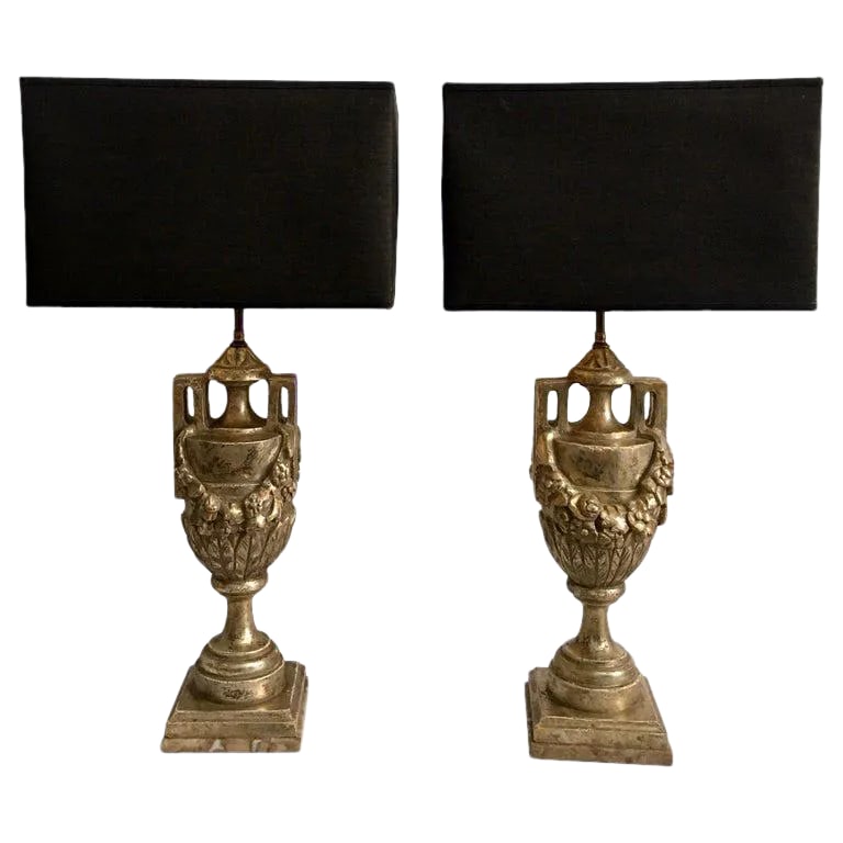 French Neoclassical Style Carved Silver Giltwood & Marble Draped Urn Lamps- A Pair: Highly detailed pair of French neoclassical style silver leaf giltwood urn lamps featuring hand carved draped foliate garland motifs. These Louis XVI style lamps are mounted on marble plinth bases