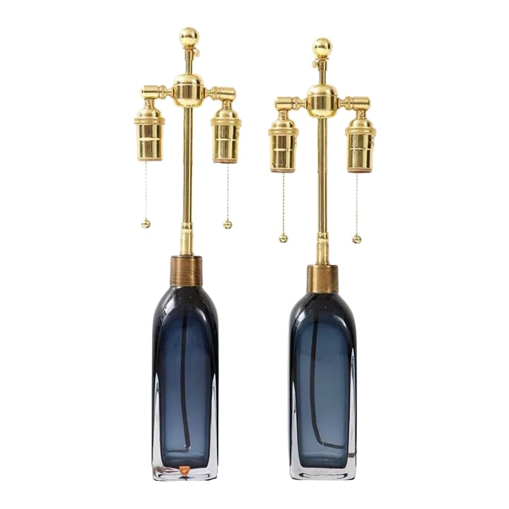 Pair of Orrefors Sapphire Blue Lamps: Pair of bottle form sapphire blue crystal lamps with adjustable polished brass double clusters and silk rayon cords. The height to the top of the glass is 8.75" and an overall height of 20.5" to the f