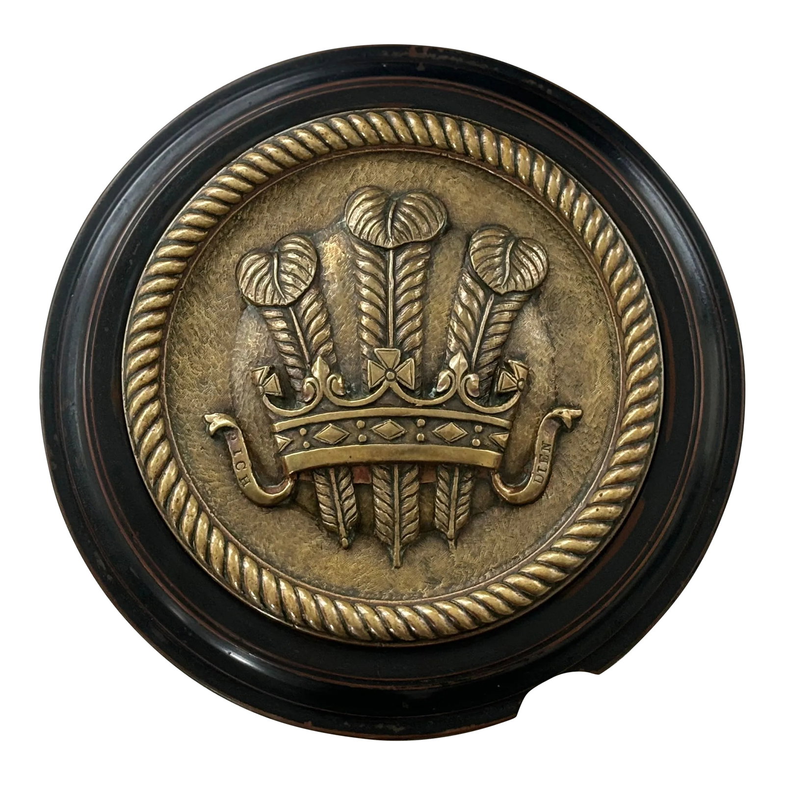 Early 20th Century Prince of Wales Tompion Plaque: Cast in brass with the Prince of Wales Feathers issuing from a crown flanked on ribbons with the motto ICH DIEN, meaning "I Serve". It is mounted on moulded backing, likely made of bakelite. It is