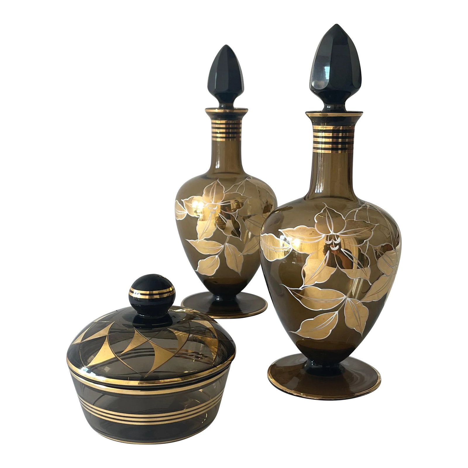 Mid 20th Century German 22K Gold, Enamel & Smoke Glass Liquor Decanter Bottle Set - 3 Pieces: Lustrous German Mid Century smoke glass decanter set , finely hand decorated with 22K gold and enamel. Set includes two decanters with faceted dark smoke glass stoppers and a covered glass dish. The