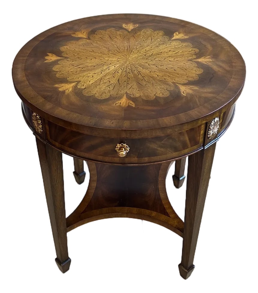 Maitland Smith Round End Table With Single Drawer: Elegant beautifully made round end table by Maitland Smith having a mix of woods, inlaid in a gorgeous decorative flower motif with bronze finish knobs, single drawer, and lower tier. TS Condition: