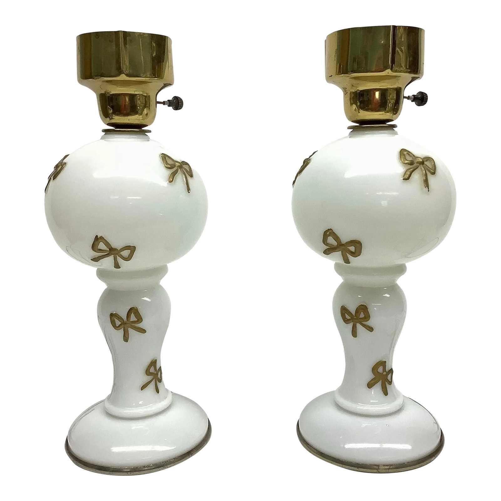 Mid Century Original White and Gold Opaline Glass Table Lamps - A Pair: This gorgeous table lamp is made of milk glass with a brass metal top, ready to hold a shade of your choice. The lamps feature painted 3D bows of gold throughout the body. It is an electric lamp, like