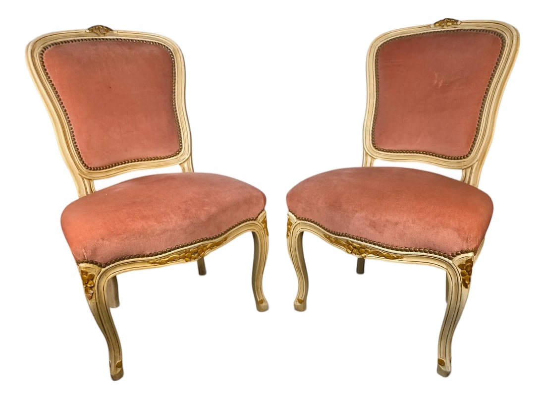 Vintage Pair of French Provincial Louis XV Style Blush Pink Velvet Accent Chairs: A charming pair of vintage French Provincial Louis XV-style accent chairs featuring gracefully carved cabriole legs, a distressed cream-painted finish with hand-highlighted gilt floral accents, and