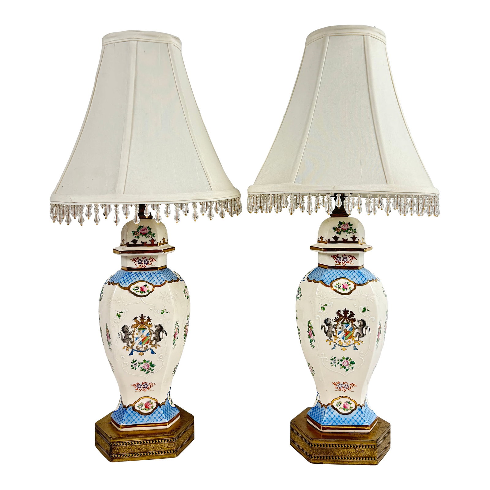 Mid 20th Century Pair of Vintage Hand Painted Porcelain Table Lamps With Lion Crest and Brass Base: Beautiful pair of Hand Painted Porcelain Table Lamps with Lion Crest and detailed Brass Base. Other side shows a floral bouquet. Amazing details throughout. Shades are adorned with clear, plastic bead