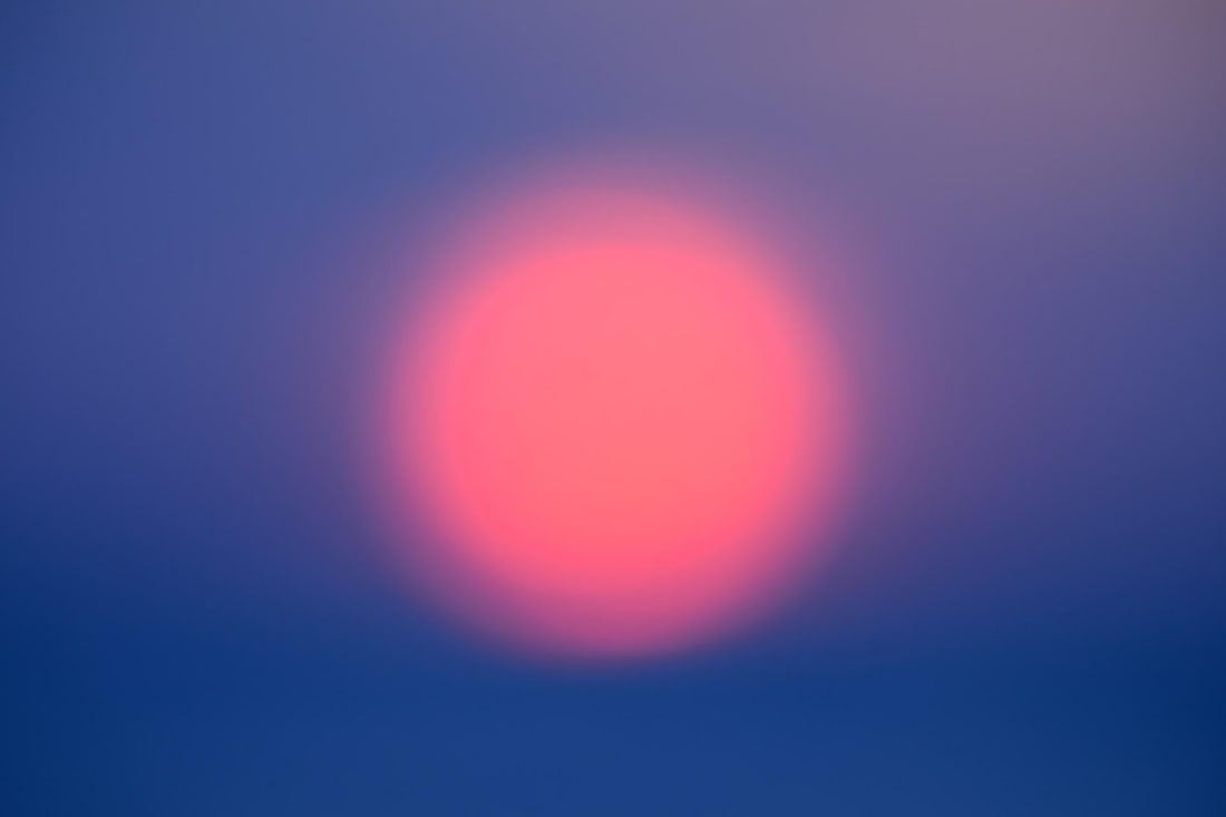 A Farewell to Day 6.1 by Tal Paz-Fridman | Photography Soft-focus sunset over the horizon.: This photograph captures a soft, ethereal sunset, where the sun appears as a glowing, pink orb against a gradient of deep blues and purples. The blurred edges create a dreamlike quality, evoking a sen