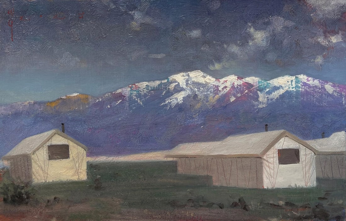 Sangre de Cristo Mountains by Diego Glazer | Oil on Board Landscape with mountains and buildings: This artwork presents a serene view of the Sangre de Cristo Mountains, their snow-capped peaks contrasting against a deep, moody sky. Two simple structures sit in the foreground, their muted colors