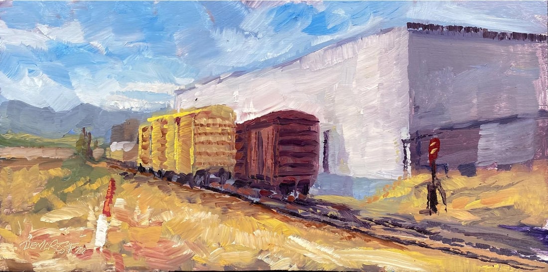 Trackside 2 by Delton Demarest | Oil on Board Painting of train cars near a building: Trackside 2 captures a serene moment at a railway yard, where weathered freight cars stand against a backdrop of soft blue skies and muted industrial structures. The artist employs bold, expressive br