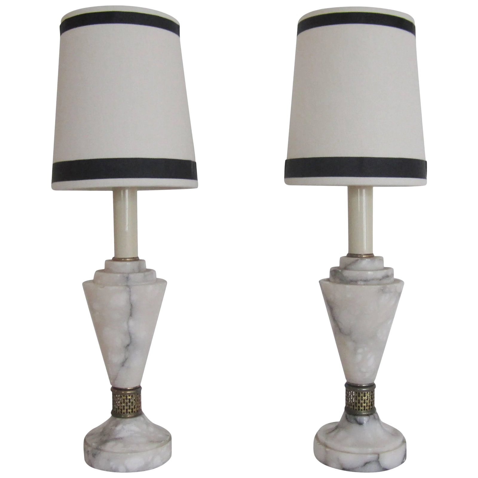 Art Deco White Carrara Marble Table or Bedside Lamps, Pair: A beautiful pair of European Art Deco Carrara marble bedside/nightstand table lamps with brass detailing. Lamps are solid marble predominately white with black and grey veining. Lamps are in fine