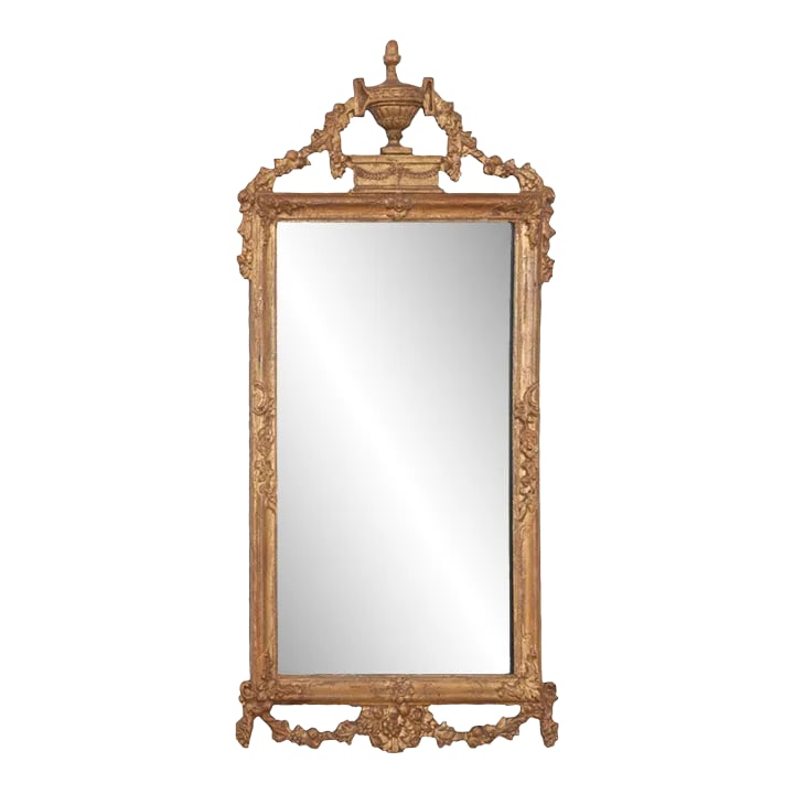 French 18th Century Louis XVI Petite Mirror: Beautifully hand-carved, this French giltwood mirror is overflowing with period details of the 18th century. A triumphant carved urn with floral garland forms a kind of pediment at the top of the fram