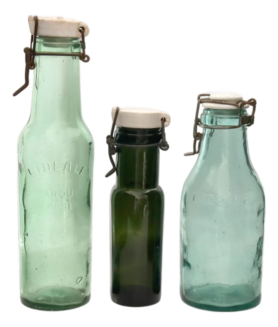 Antique French Swing Top Food Storage Bottles: This collection of antique French swing top bottles features "L'Ideale" glass with embossed branding and ceramic stoppers. Crafted in varying shades of green and blue, these bottles offer rustic