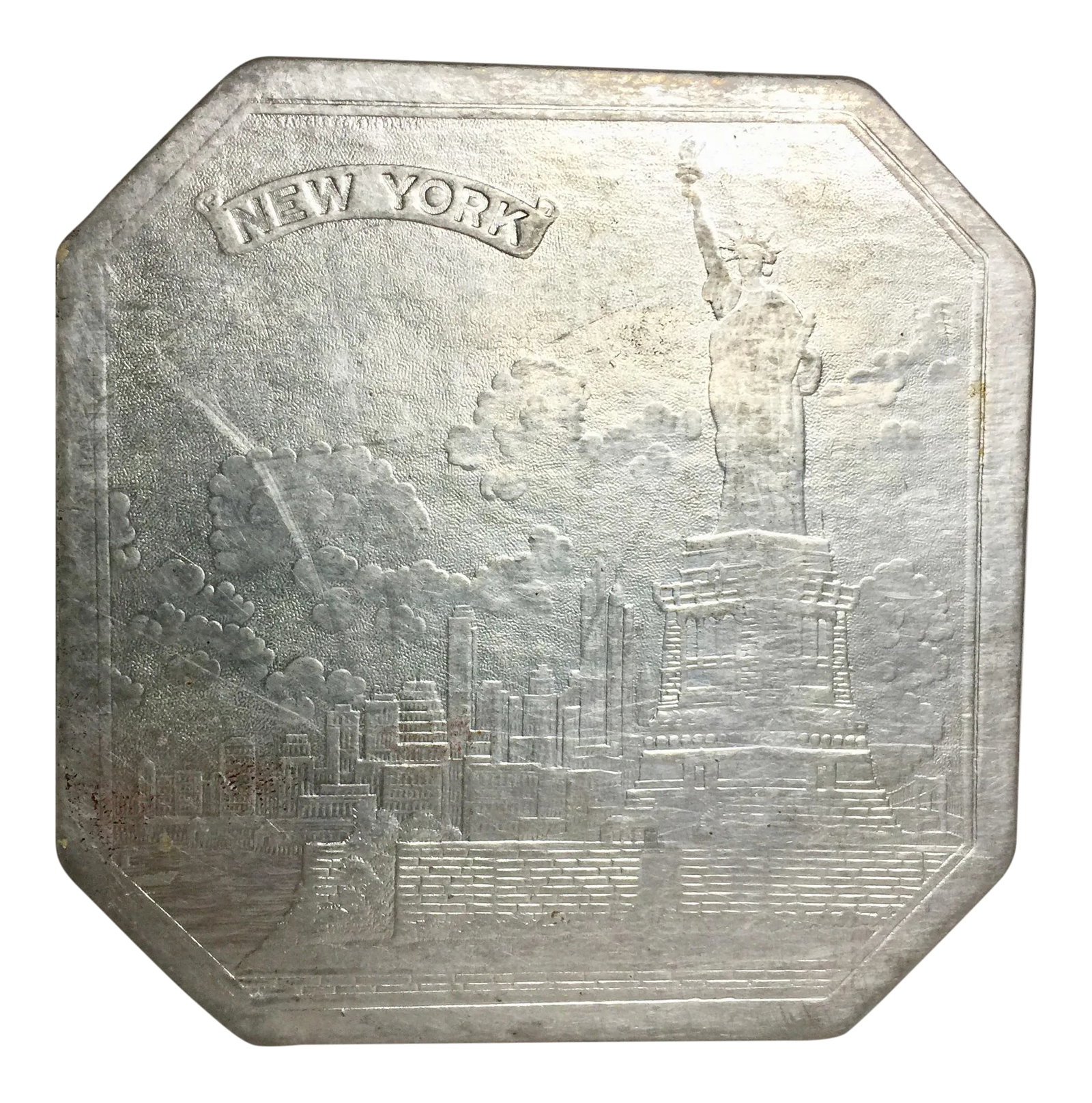 Pressed Embossed Foil Trivet New York City: Vintage pressed embossed foil trivet showing the Statue of Liberty, Brooklyn Bridge and downtown Manhattan. c. 1940s. Backed with textured blue paper. Octagonal shape. Well used with some surface and