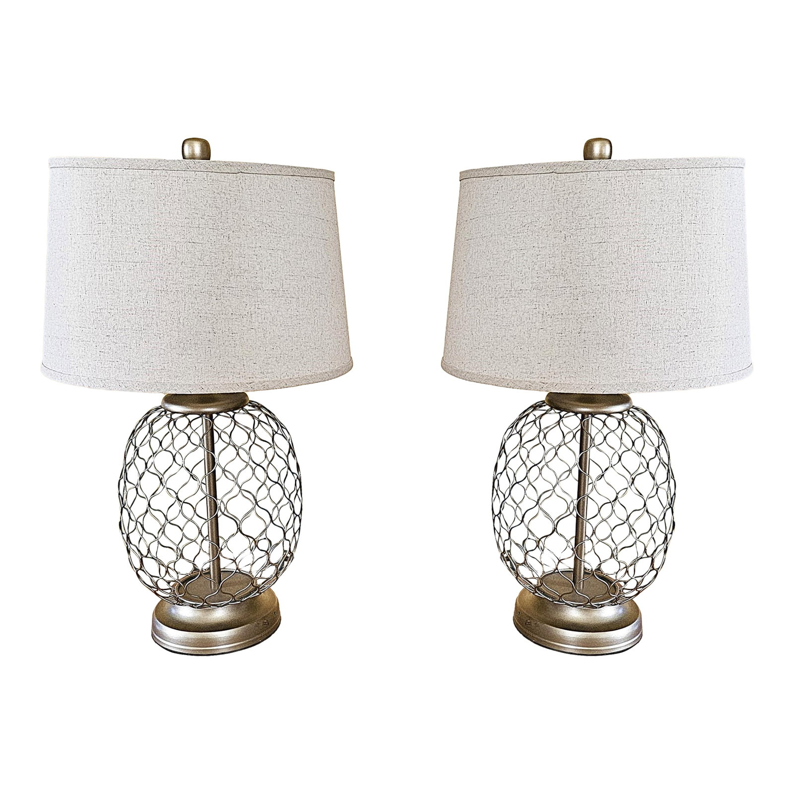 Pair of Modern Industrial Cage Metal Table Lamps With Linen Shades: This stunning pair of table lamps features an open metal cage base in a brushed silver-tone finish, paired with elegant off-white linen drum shades. The intricate wire design creates a contemporary