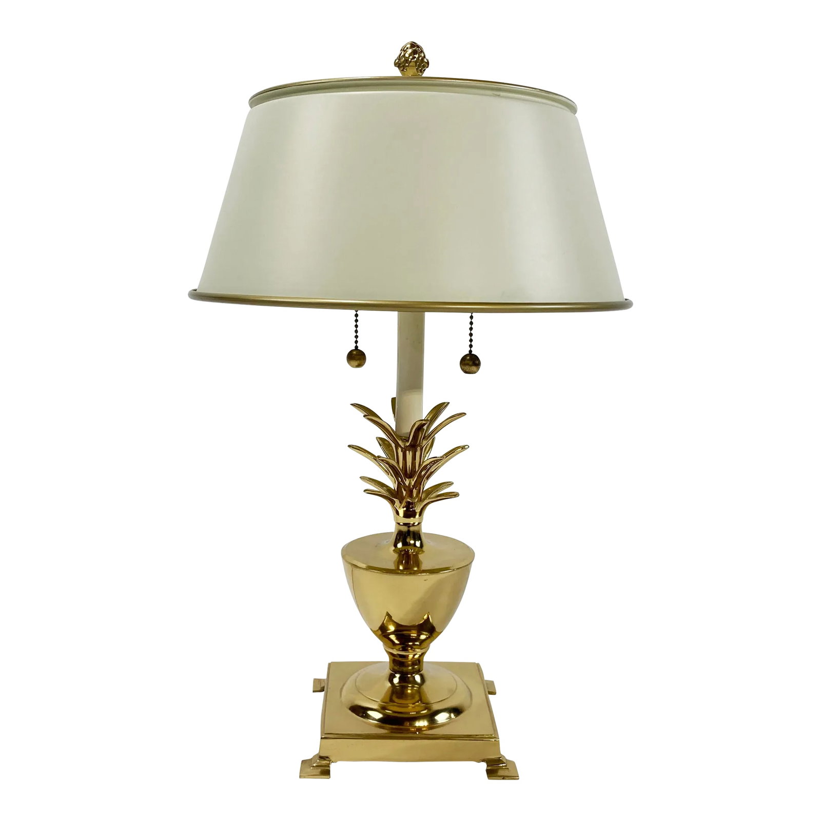 Vintage Bombay Brass Pineapple Table Lamp W/ Tole Shade: Vintage brass pineapple lamp with ivory metal tole shade. Lamp has double sockets with separate brass pulls for each bulb. Shade measures 12"W at base and 6"H. Brass pineapple finial to top lamp.