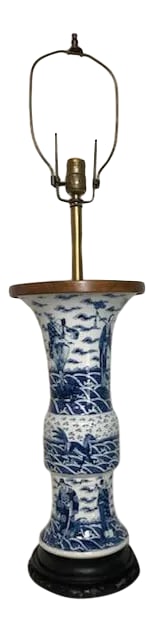 Late 19th Century Chinese Blue & White Porcelain Lamp: This Chinese porcelain Gu vase, has been wired as a lamp. The lamp features a custom walnut top and a Chinese carved wooden base. The painted details on the lamp depict people and animals in various