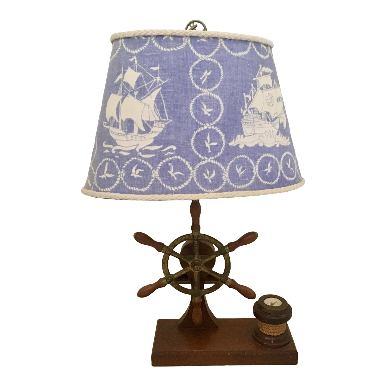 Vintage Mid-Century Ship Wheel Table Lamp With Brass Compass: Vintage Ship's Wheel table lamp with aged brass wheel, solid wood base, and working brass compass. Lamp includes oval, linen shade in a blue & ivory nautical print, with ivory rope trim around the per