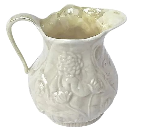 Antique Porcelain Floral Creamer: Antique; 1900-1910, porcelain Bleeker floral creamer with handle. Depicts floral designs in bas relief style around outside surface. Marked with Bleeker logo on the underside. Minor wear. Condition: