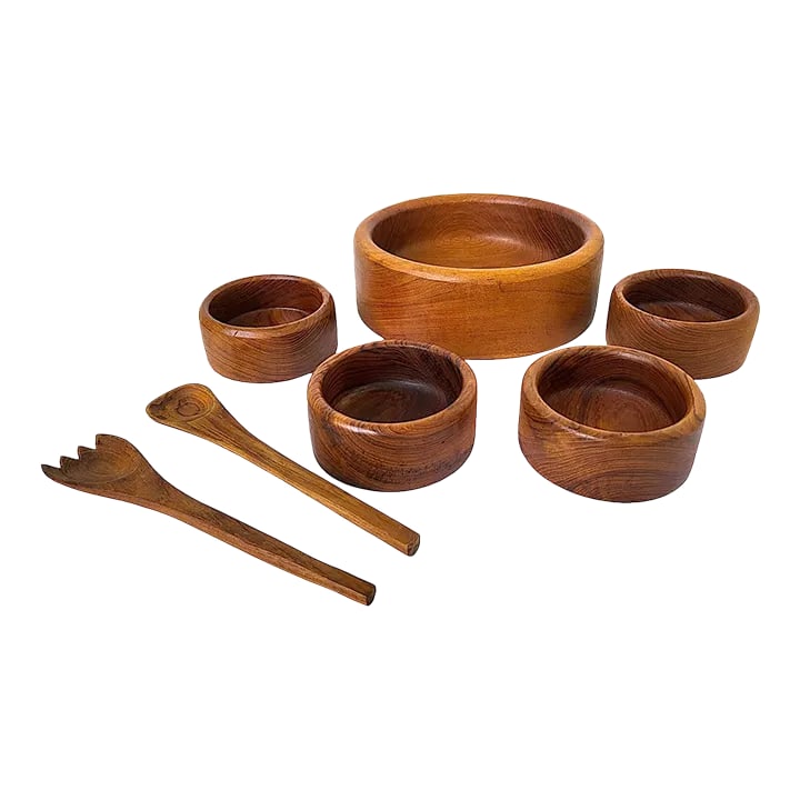 1970s Teak Wood Salad Bowls and Serving Utensils, Set of 7: Offered is a vintage mid 1970s set of Goodwood brand Teak salad bowls made in Thailand and a pair of serving utensils. Carved from a solid piece of wood, the large serving bowl measures 12" in diamete