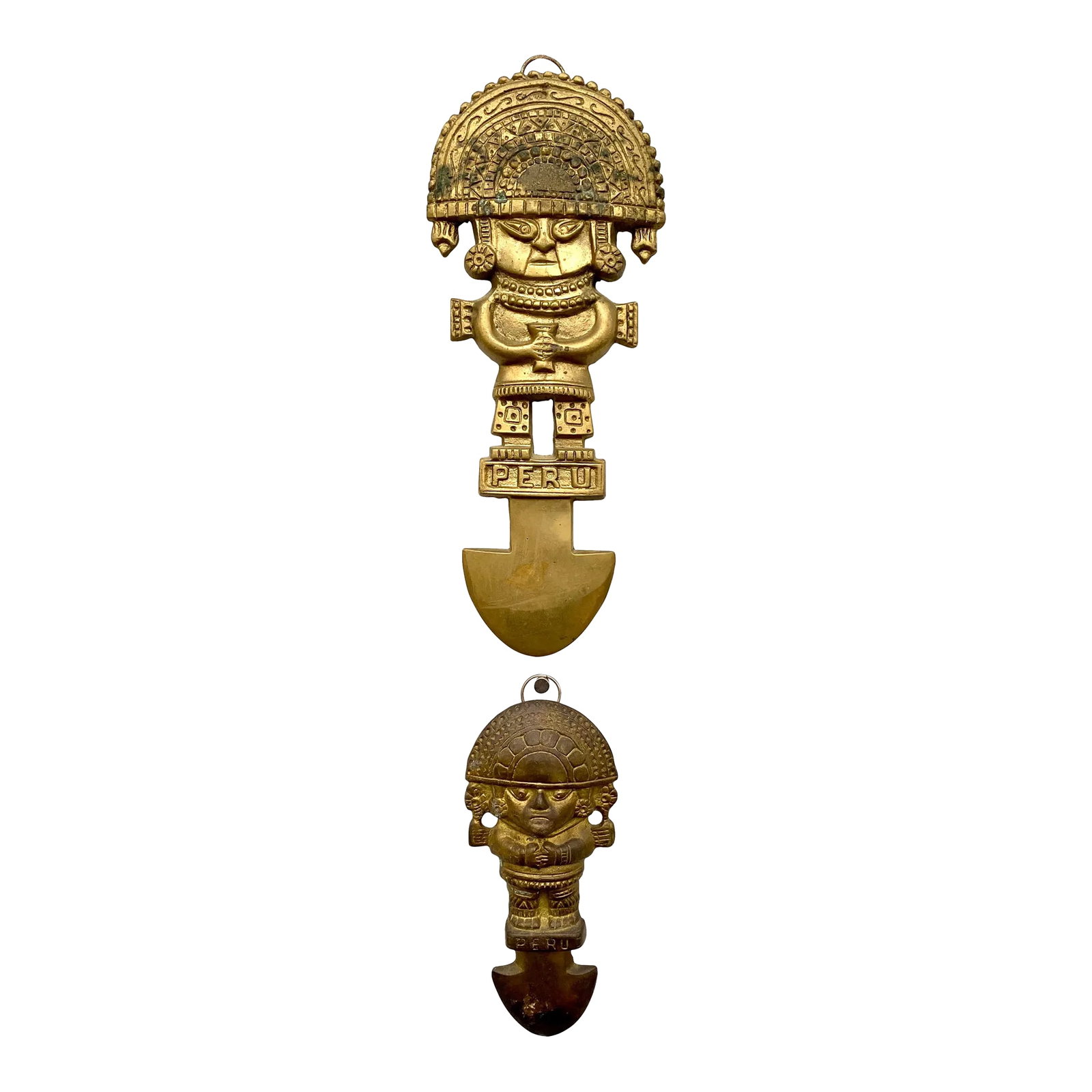Mid 20th Century Peruvian Brass Sculptural Wall Art- Set of 2: Two hanging tribal Peruvian figure wall art pieces. Cast and brass each has Peru written on it and has a figure with a headdress standing atop what looks like a shovel or spearhead. The large one