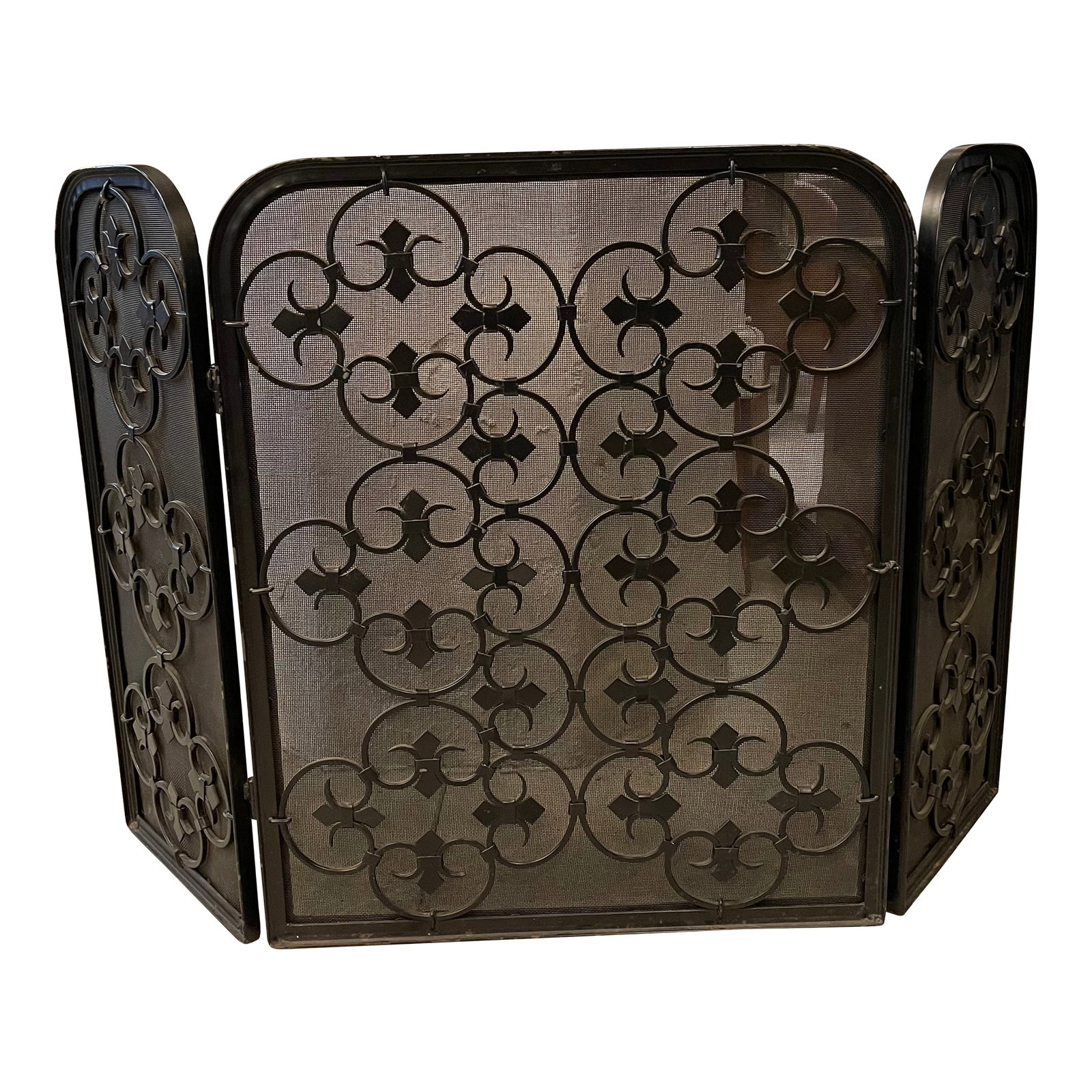 Mid 20th Century Hollywood Regency Scrolled Iron and Mesh Trifold Fireplace Screen: This elegant Hollywood Regency trifold fireplace screen is as practical as it is decorative. Constructed with fine mesh backing, it features an arched, black wrought iron frame adorned with symmetrica