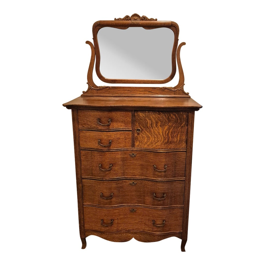 Early 20th Century Victorian-Era Serpentine Highboy Dresser: This is a Victorian-era serpentine highboy dresser crafted from quarter-sawn "tiger" oak, featuring a carved crest and a swivel mirror. Materials and Style: The piece utilizes quarter-sawn oak, which