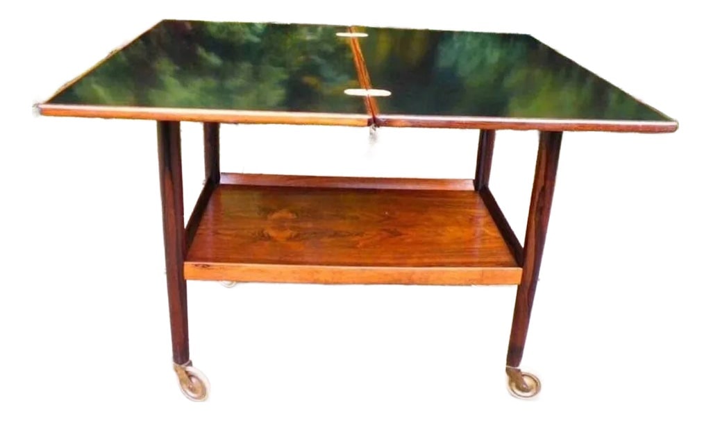 1960s Danish Rosewood Tea Trolley: A teak two-tier tea bar cart serving/drinks trolley with large easy rolling rubber rimmed casters. The top slides to one side, turns 90 degrees and opens up to double the size. Superb curved lines and