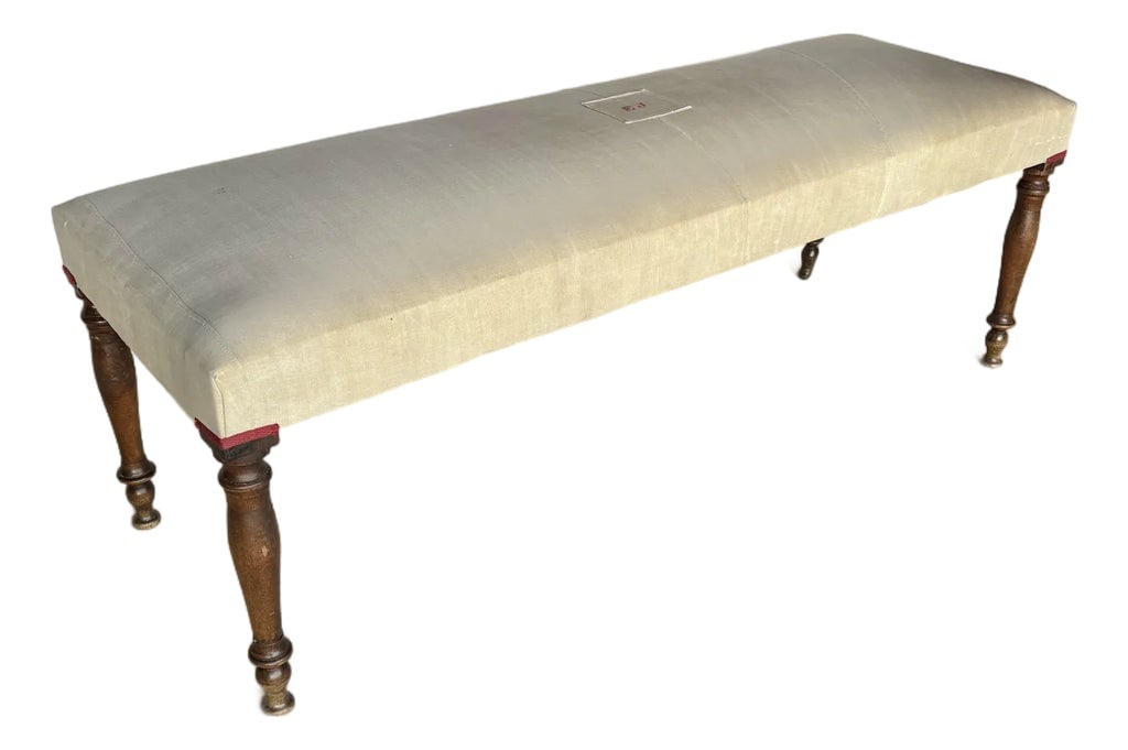 Early 20th Century French Walnut and Antique Linen Upholstered Bench: Found in the South of France, this Early 20th Century French Walnut and Antique Linen Upholstered Bench was crafted in the early 1900's. The piece features an antique French linen upholstered top rest