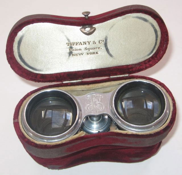 “Tiffany, NY” Mother-of-Pearl Opera Glasses + Case: c1890. Measures 2 1/2” tall, 4 1/8” wide, 1 1/4” deep (6.4 x 10.5 x 3.2 cm). Burgundy velvet case with braided strap.