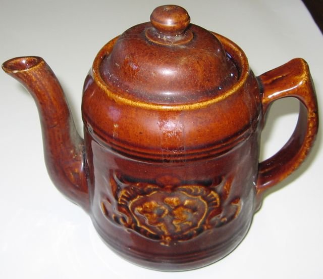 “Foley Pottery” Earthenware Tea Pot Saint John NB: Cherub design. Measueres 6 ½” tall, 4” diameter,diameter, 7” handle to spout (16.5, 10.2, 17.8 cm). Includes lid. Collection of Pat & Connie Kent, former operators of Granary Antiques, Fairfiel